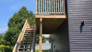 A wooden deck with a staircase leading to a balcony, adjacent to a building with horizontal siding.