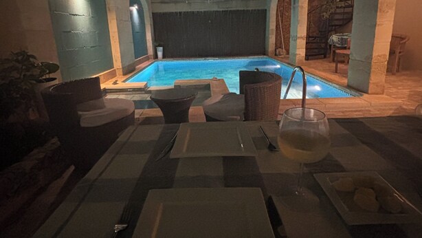 Zona de menjador a la piscina amb una taula preparada per a dues persones, una copa de vi i un plat de menjar.