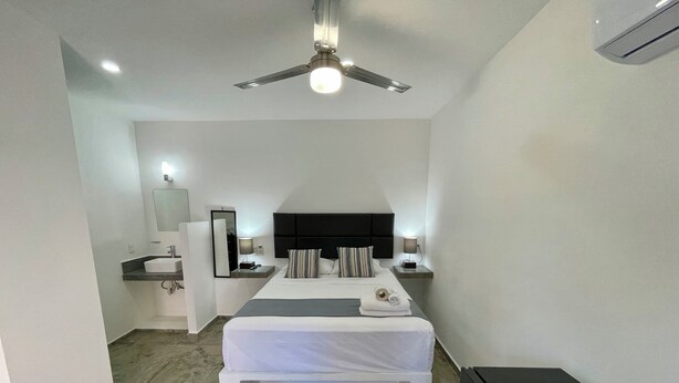 A bedroom with a bed, bedside tables, a mirror, a ceiling fan, and a black TV stand. - Lavish Studio w Kitchen Downtown (Isla Mujeres)