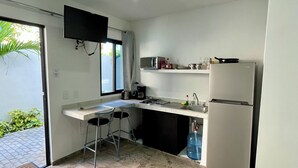 A compact kitchen with a built-in microwave, a refrigerator, and a small countertop. There are two stools and a window providing natural light. - Lavish Studio w Kitchen Downtown (Isla Mujeres)