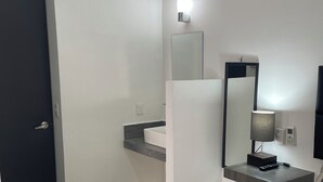 A modern bathroom with a dark door, a white sink, a mirror, and a bedside table with a lamp. - Lavish Studio w Kitchen Downtown (Isla Mujeres)