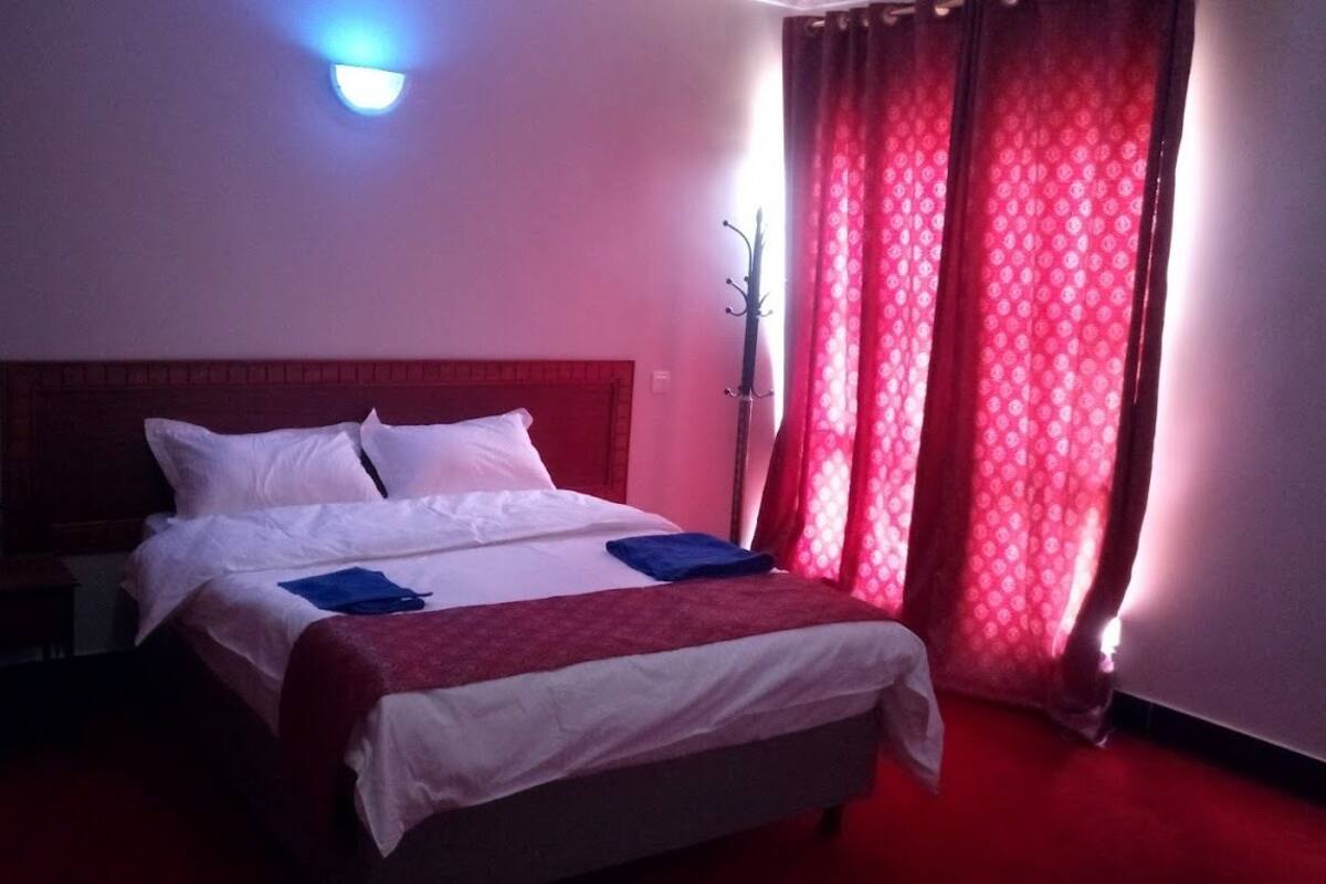 A hotel room with a bed, a nightstand, and a coat rack.