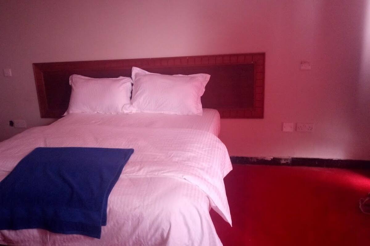 A bed with white bedding and a blue blanket, a wooden headboard, and a red wall.