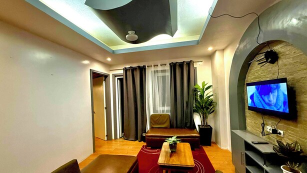A modern living room with a sofa, a coffee table, a TV mounted on a stone wall, and a potted plant. - The Terrace condominium baguio city (Baguio)