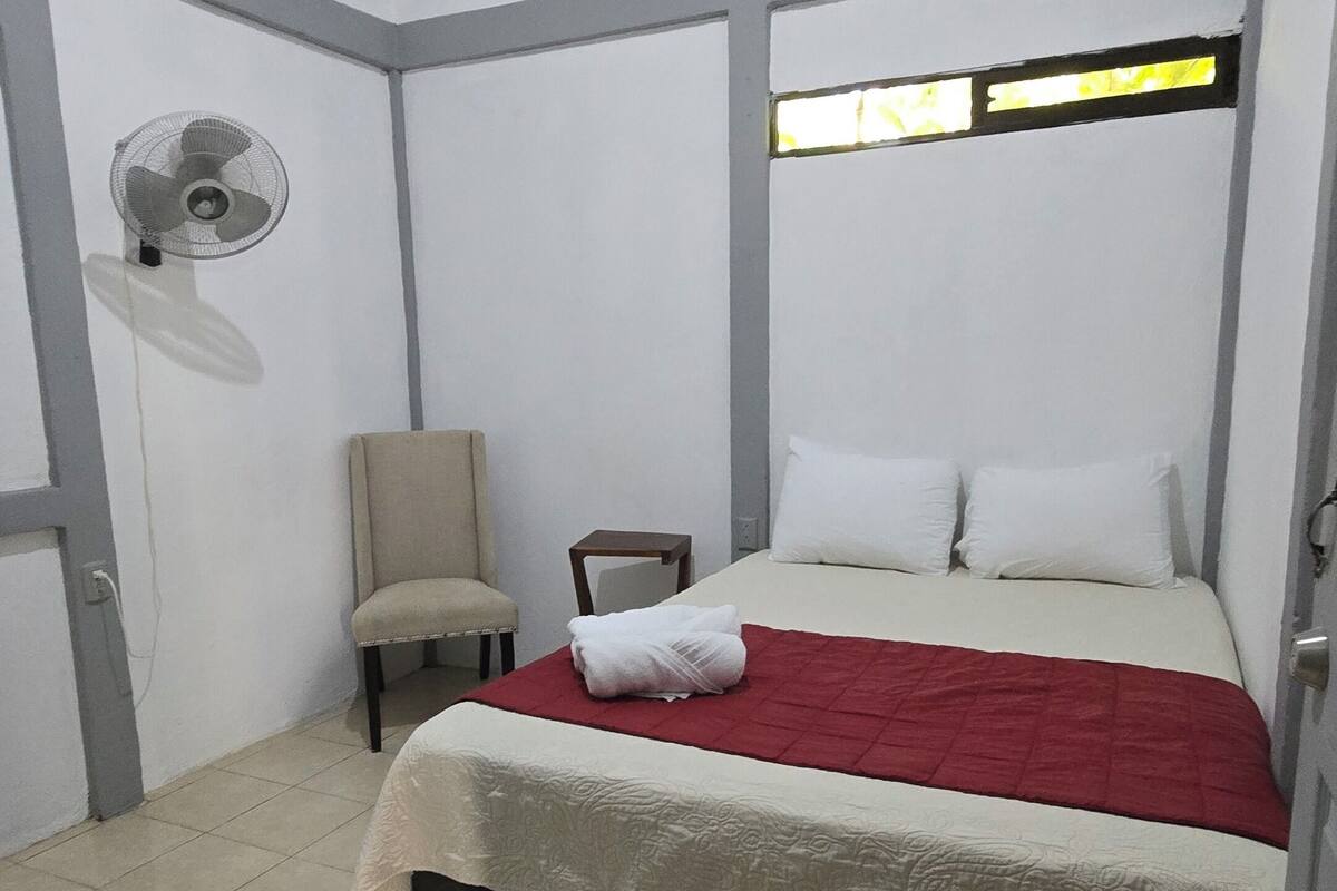 A bedroom with a bed, a chair, a fan, and a window.