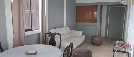 A dining area with a table and chairs, a sofa, a ceiling fan, and a window with curtains.
