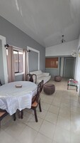 Un comedor con una mesa y sillas, un sofá, un ventilador de techo y una ventana con cortinas.