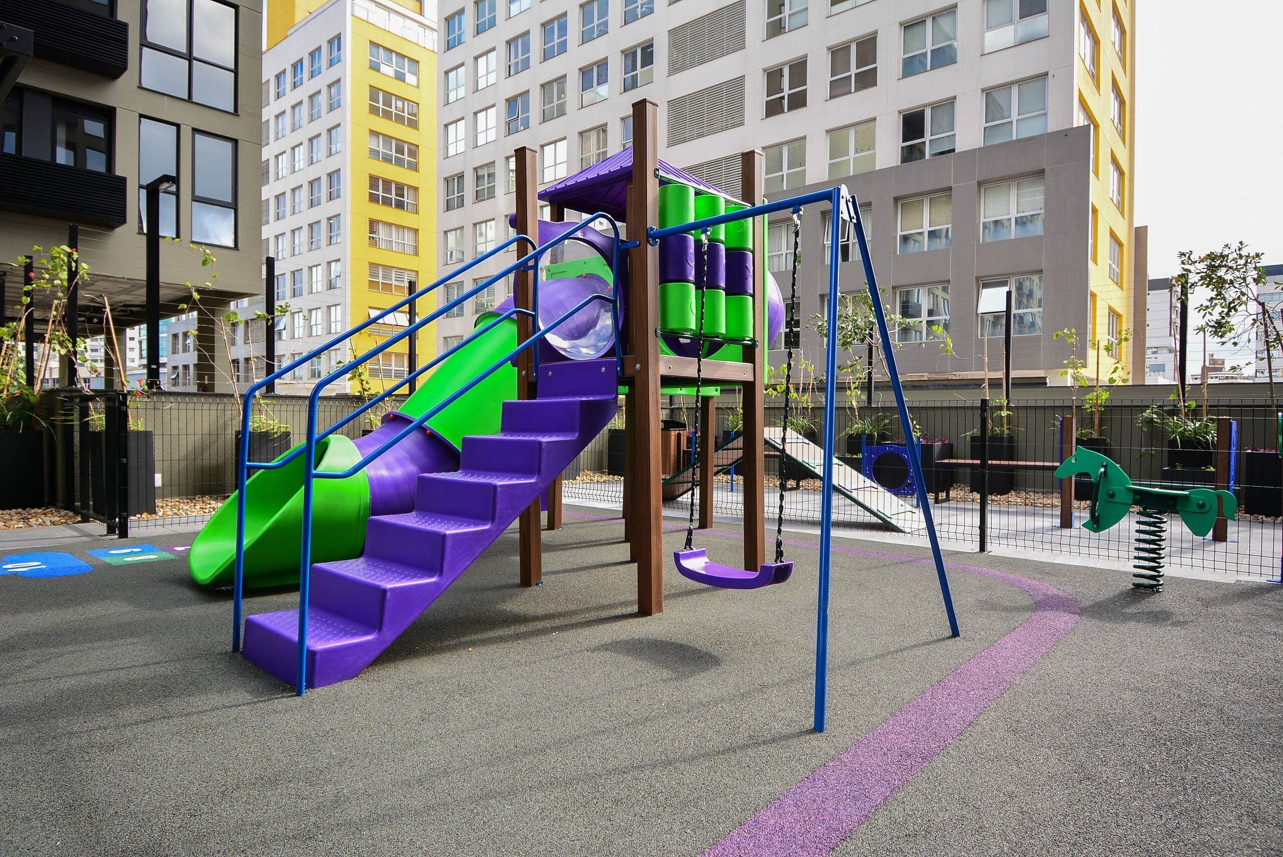 A playground with a purple slide, green and purple climbing area, and swings.
