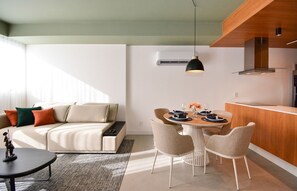Una sala de estar moderna con un sofá, una mesa de comedor y sillas. Cuenta con una zona de cocina con mostrador y una lámpara colgante.