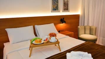 A hotel room with a bed, a bedside table with a lamp, a chair, and a tray with food and drinks.