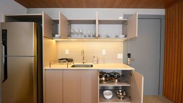 A compact kitchen with a built-in refrigerator, a sink, and open cabinets revealing dishes and cookware.