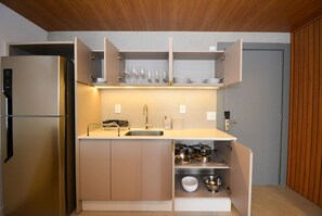 Una cocina compacta con un refrigerador integrado, un lavamanos y armarios abiertos que muestran vajilla y utensilios de cocina.