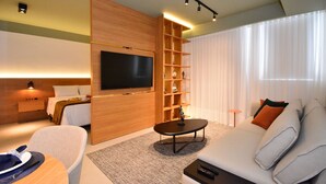 Une chambre d’hôtel moderne équipée d’un téléviseur à écran plat, d’un canapé, d’une table basse et d’une bibliothèque.