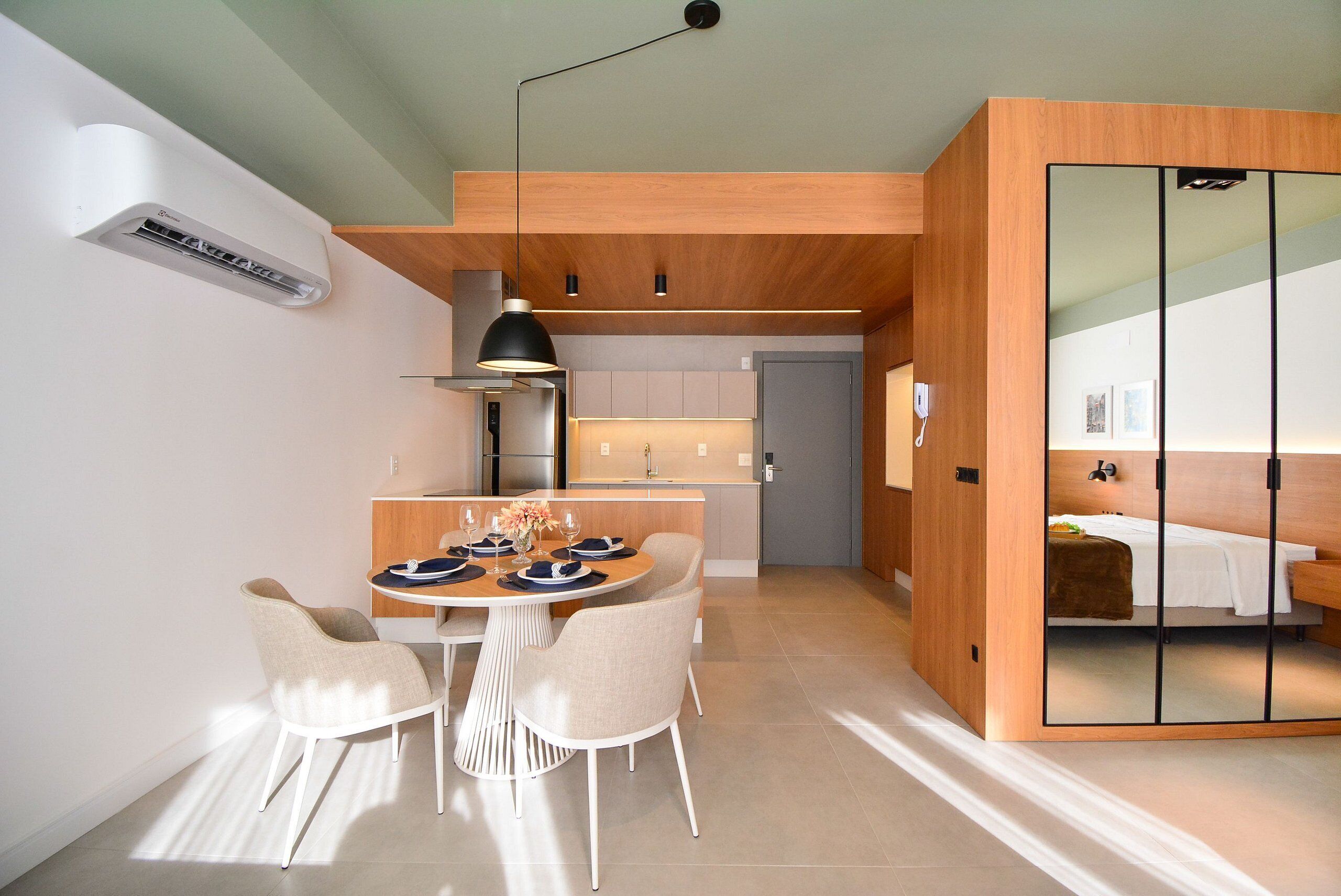 Una cocina moderna con armarios de madera, un comedor con mesa y sillas redondas, y un dormitorio con puerta corredera.