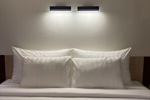 Una cama con ropa blanca y dos lámparas de pared encima.