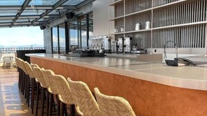 Zona de bar moderna con una barra larga, sillas de mimbre y vistas de la ciudad.