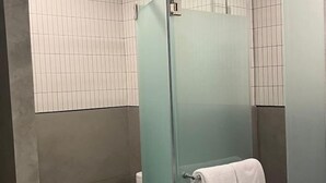 Ducha con cerramiento de vidrio y una toalla colgada del picaporte.