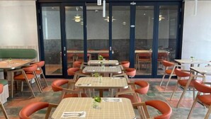 Un restaurante con varias mesas y sillas, puerta de vidrio y suelo de baldosas.