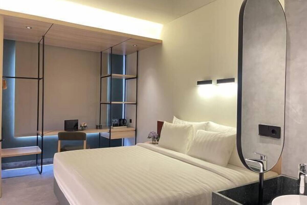 Una habitación de hotel moderna con una cama, un escritorio, una silla, un espejo y un baño.