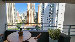 A balcony with a round table and chairs, a potted plant, and a view of high-rise buildings. - Comfortable studio apartment in Perdizes - Allianz Parque with pool and rooftop. (São Paulo)