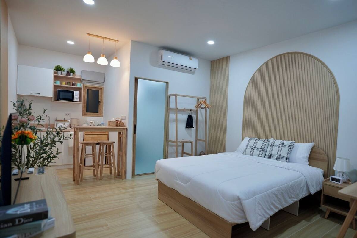 Une chambre d’hôtel moderne avec un lit en bois, une petite kitchenette, un bureau et une armoire.
