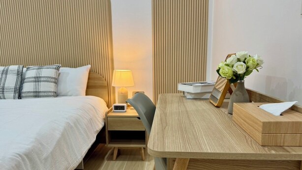 Ein Hotelzimmer mit Bett, Nachttisch mit Lampe, einem Sessel, einem Schreibtisch mit Blumenvase und einer Nachttischuhr.
