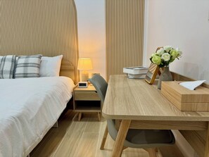 A hotel room with a bed, bedside table with a lamp, a chair, a desk with a vase of flowers, and a bedside clock. - The Cozy Haus Airport (Mai Khao)