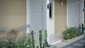 Ein moderner Außenbereich mit Sitzgelegenheit, einem Tisch, Stühlen, einer Wand mit geometrischen Mustern sowie verschiedenen Kakteen und blühenden Pflanzen.