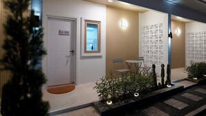 Ein moderner Hotel-Eingangsbereich mit einer Rezeption, einer Tür mit der Bezeichnung „A 005“ und einer Wand mit geometrischen Mustern.