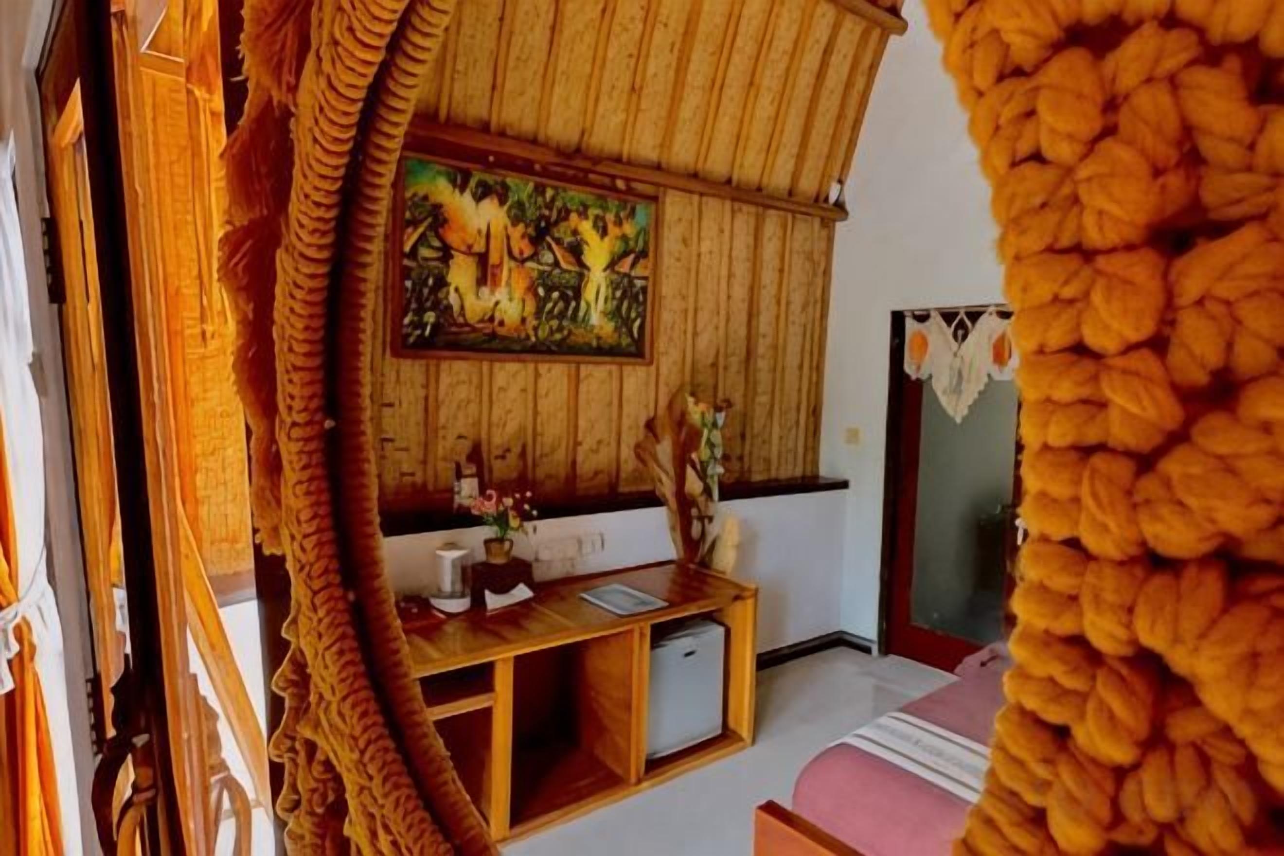 Una habitación con techo de madera, un cuadro en la pared, un escritorio con computadora y una cama con manta rosa.