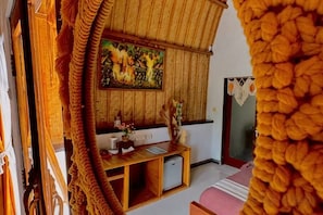 A room with a wooden ceiling, a painting on the wall, a desk with a computer, and a bed with a pink blanket. - Meket Bungalows (Bali)
