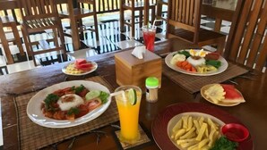 A dining table with various dishes, including a plate of fries, a salad, and a fruit bowl. - Meket Bungalows (Bali)