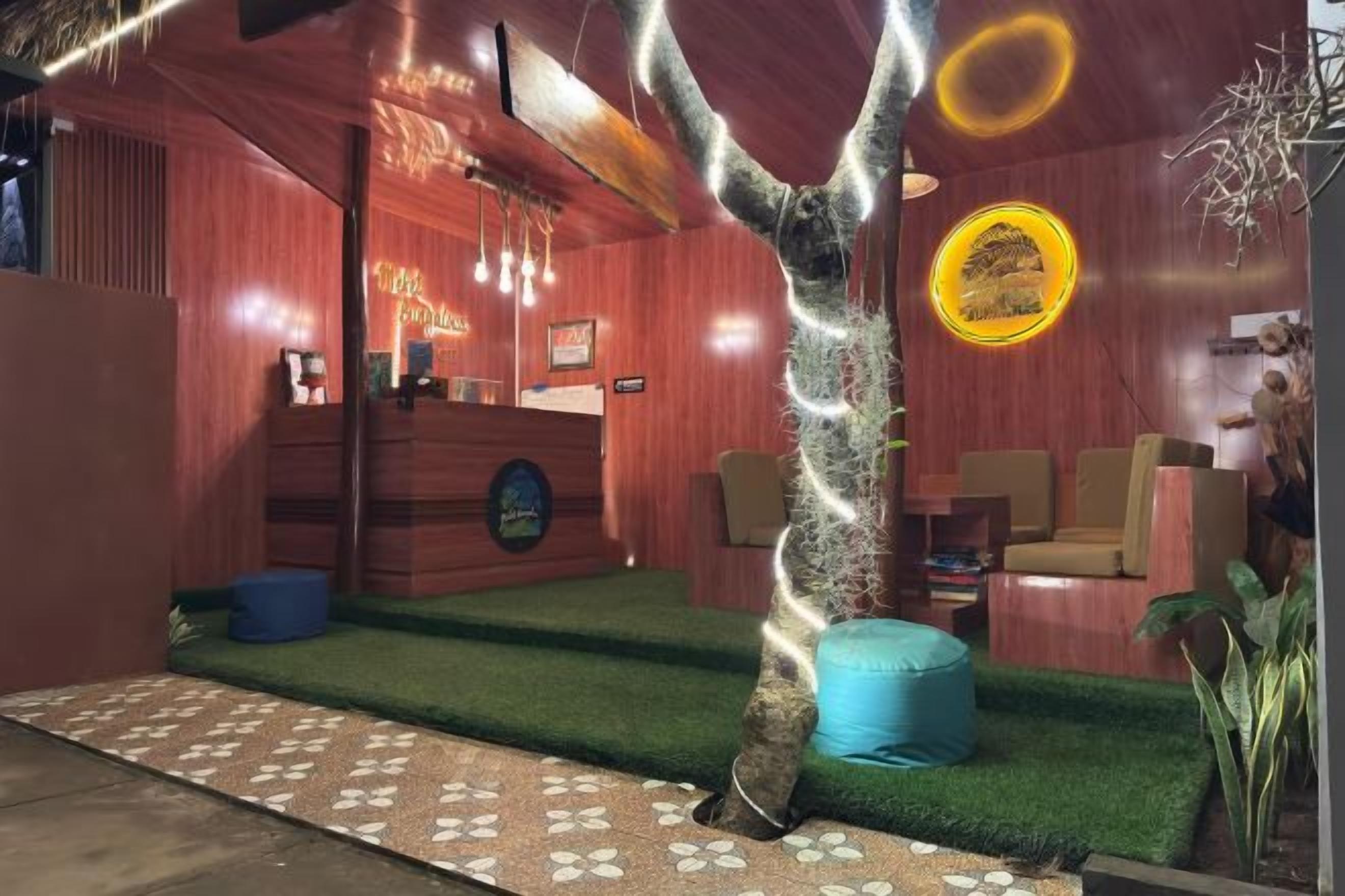 Un área de recepción con un escritorio de madera, un banco azul y un árbol con luces colgantes.