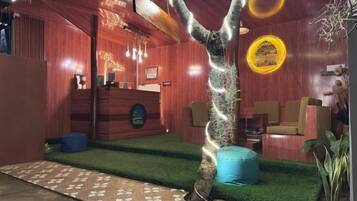 Un área de recepción con un escritorio de madera, un banco azul y un árbol con luces colgantes.