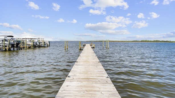 A wooden pier extending into calm water with a docked boat on the left and a clear sky above. - Wolf Bay Villas 208: Waterfront (Orange Beach)