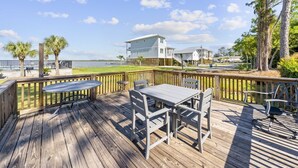 A wooden deck with a table and chairs, overlooking a body of water and a white building. - Wolf Bay Villas 208: Waterfront (Orange Beach)