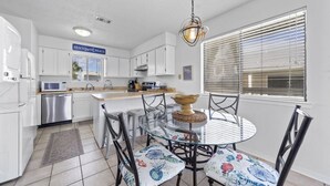 Una cocina moderna con armarios blancos, lavavajillas de acero inoxidable y una mesa redonda con sillas estampadas de flores.