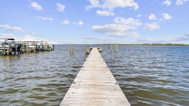 Un muelle de madera se adentra en aguas tranquilas, con un barco amarrado a la izquierda y un cielo despejado.