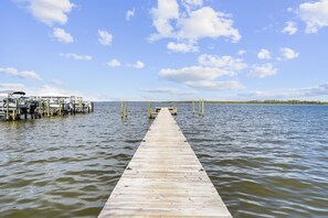 Une jetée en bois s’étendant sur une étendue d’eau calme, avec un bateau amarré sur la gauche et un ciel dégagé au-dessus.