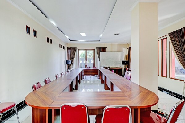 Una sala conferenze con un lungo tavolo in legno, sedie rosse e una lavagna.