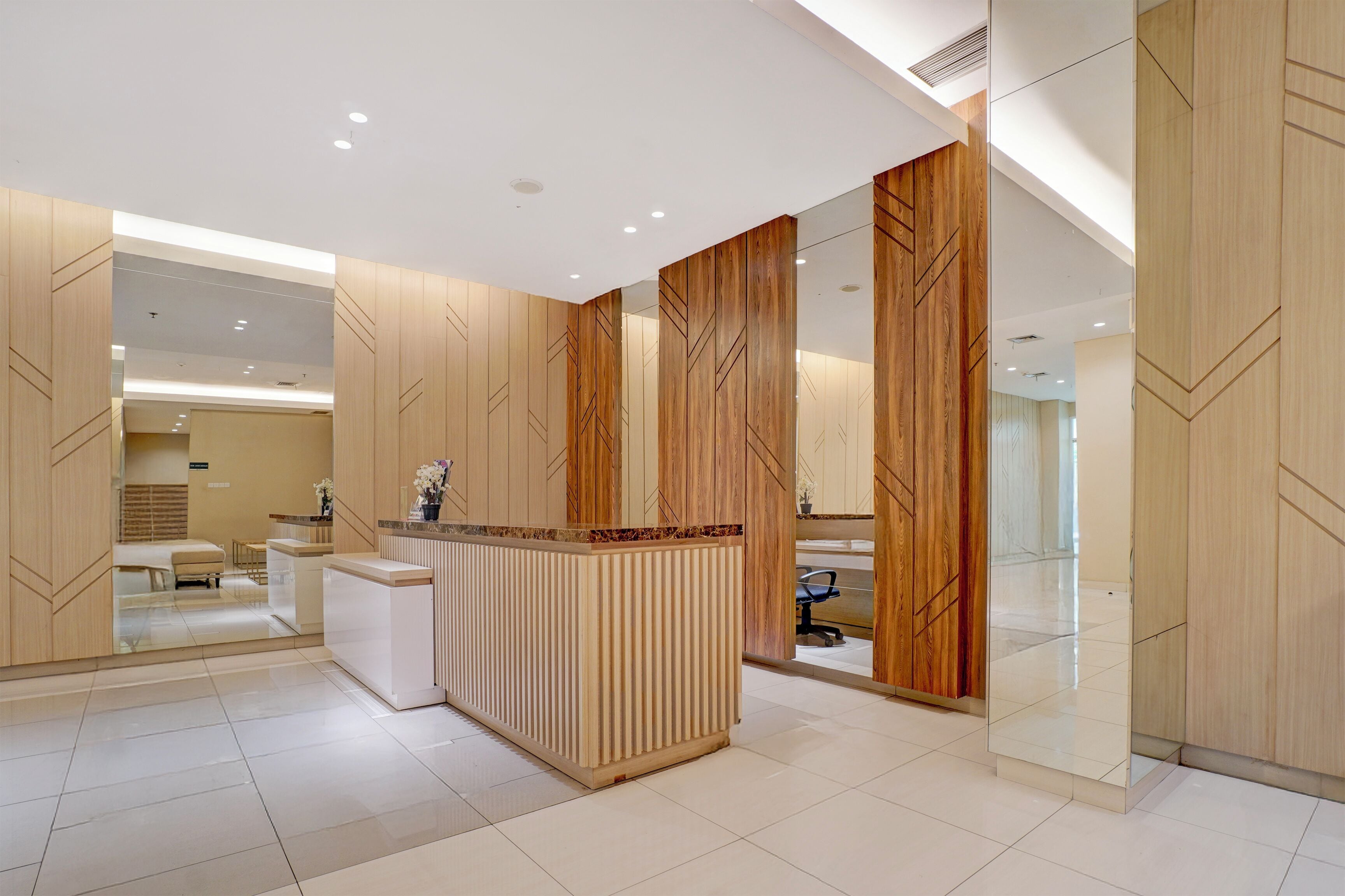 A modern hotel lobby with a reception desk, seating area, and a large mirror reflecting the space.