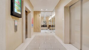 A modern hallway with a digital advertisement, an elevator, and a glass door leading to a seating area. - OYO 94837 Apartment Ekki Tower (Gunung Putri)