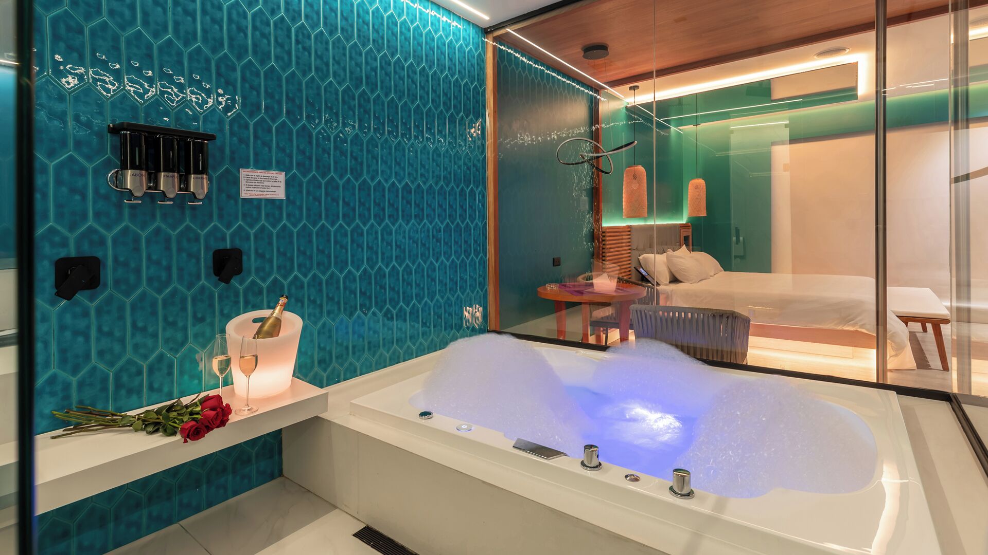 Un baño moderno con una bañera grande, una cabina de ducha de vidrio y una cama visible en la habitación contigua.