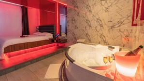 A hotel room with a bed, a second bed, a bathroom with a jacuzzi, and a bottle of champagne. - Liv Motel Ecuador (Quito)