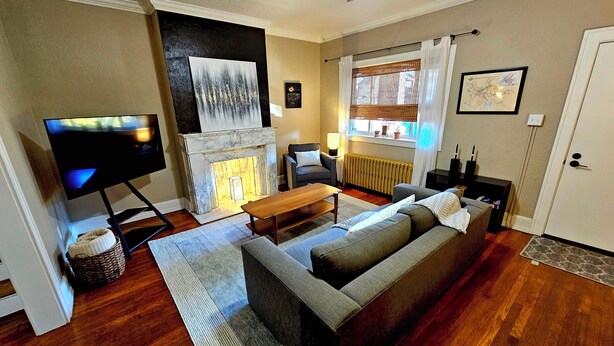 Een woonkamer met een bank, een televisie, een open haard en een raam met gordijnen.