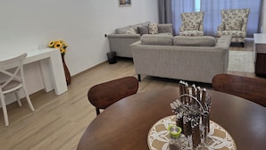 A modern living room with a grey sofa set, a dining table with a knife set, and a white desk with a vase of sunflowers. - Marina Bay Suites (Nairobi)