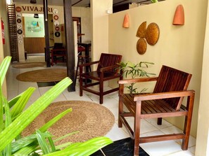 Un espace d’accueil avec des chaises en bois, une table ronde en osier et un mur orné d’assiettes décoratives et d’une enseigne.