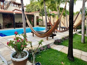 Un espace piscine agrémenté d’un hamac, de palmiers et d’une plante en pot aux fleurs roses.