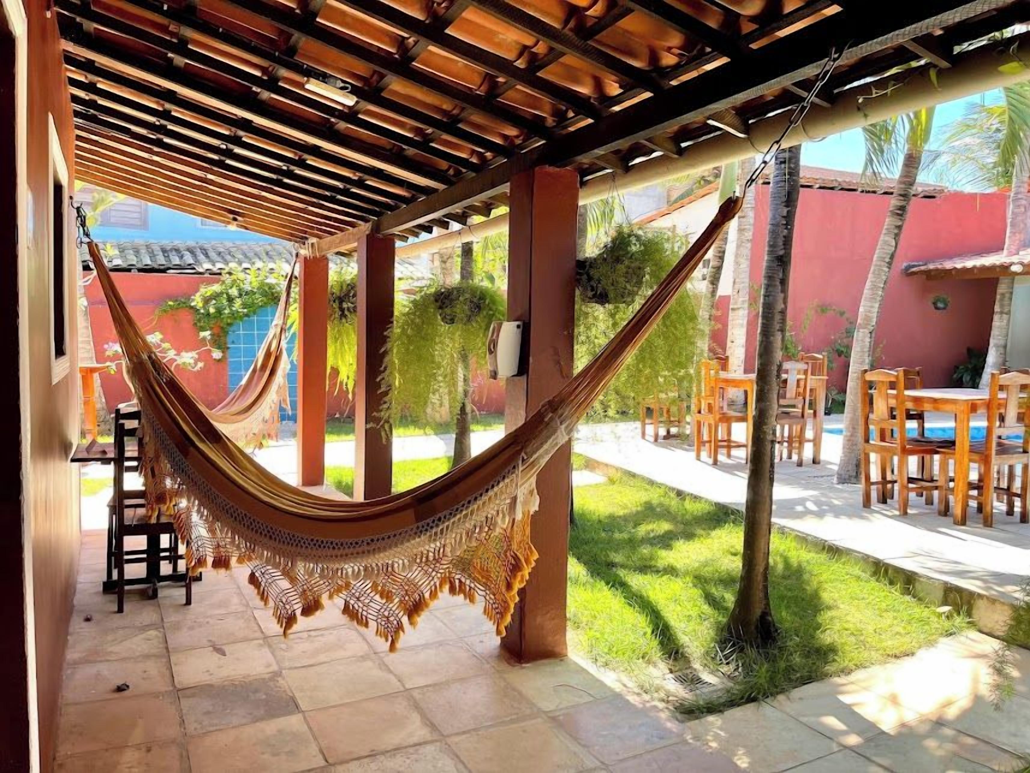 Una hamaca bajo una pérgola de madera, zona de estar al aire libre y vistas a la piscina.