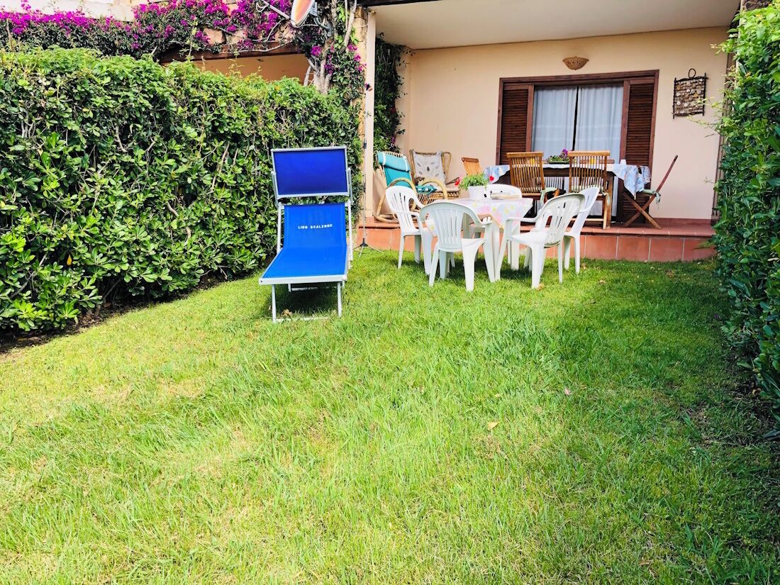 Une terrasse avec une table et des chaises, entourée d’une pelouse bien entretenue et d’une haie.